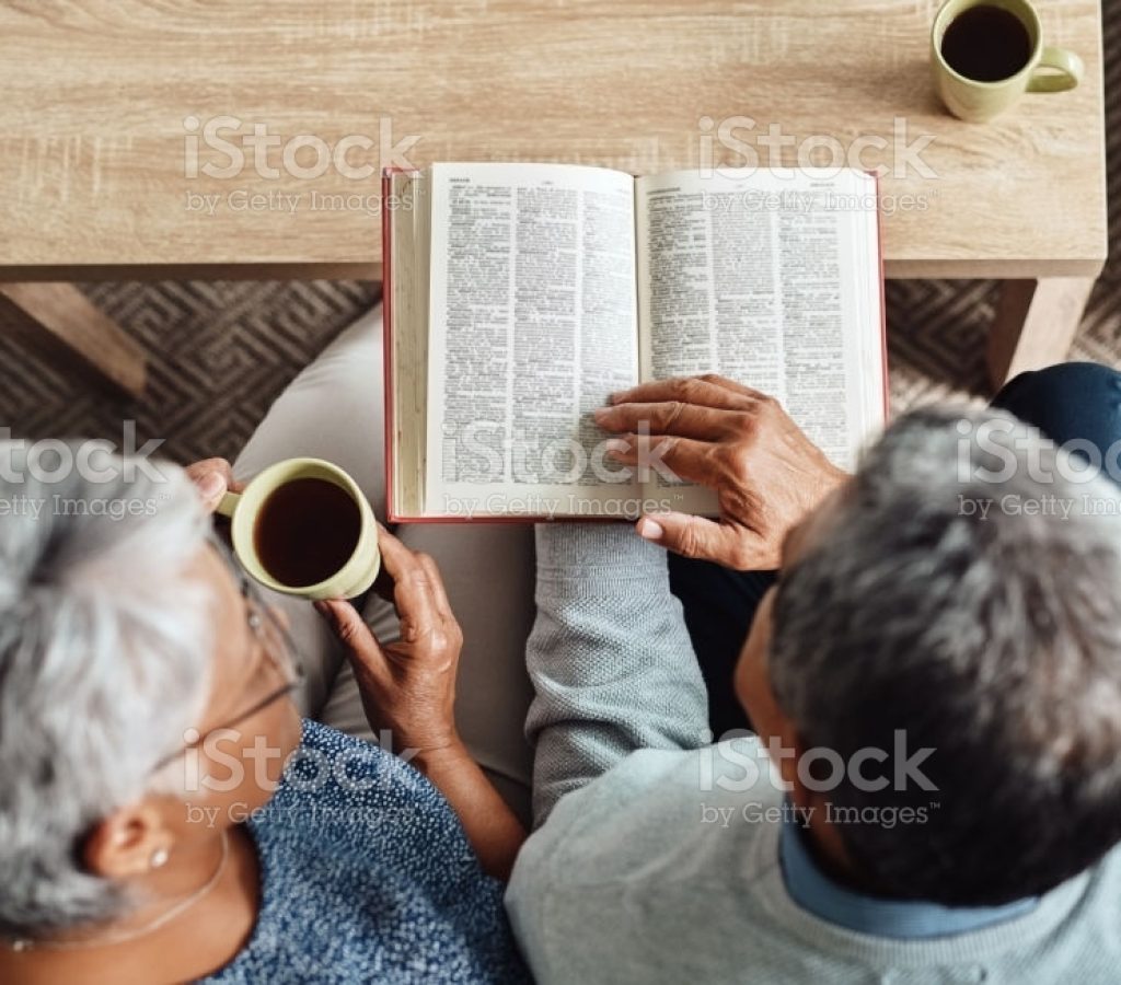 High angle shot of a relaxed elderly couple reading from the bible while drinking coffee at home during the day